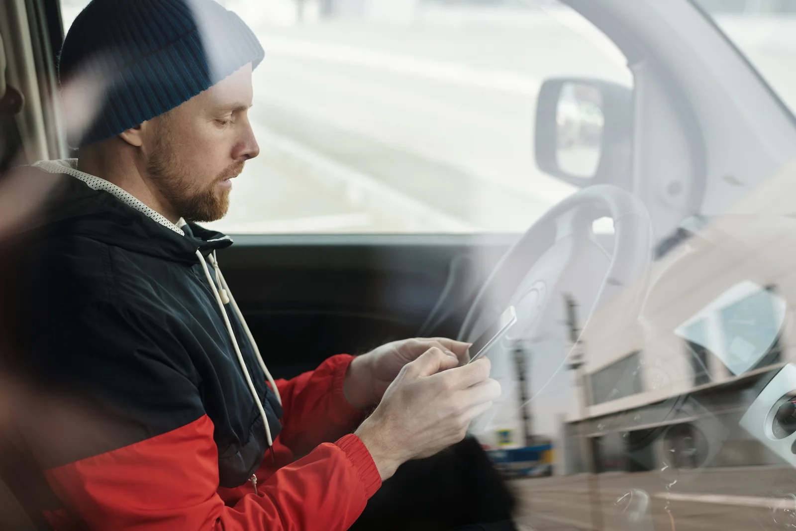 A driver using a phone in a car, seen through the side window